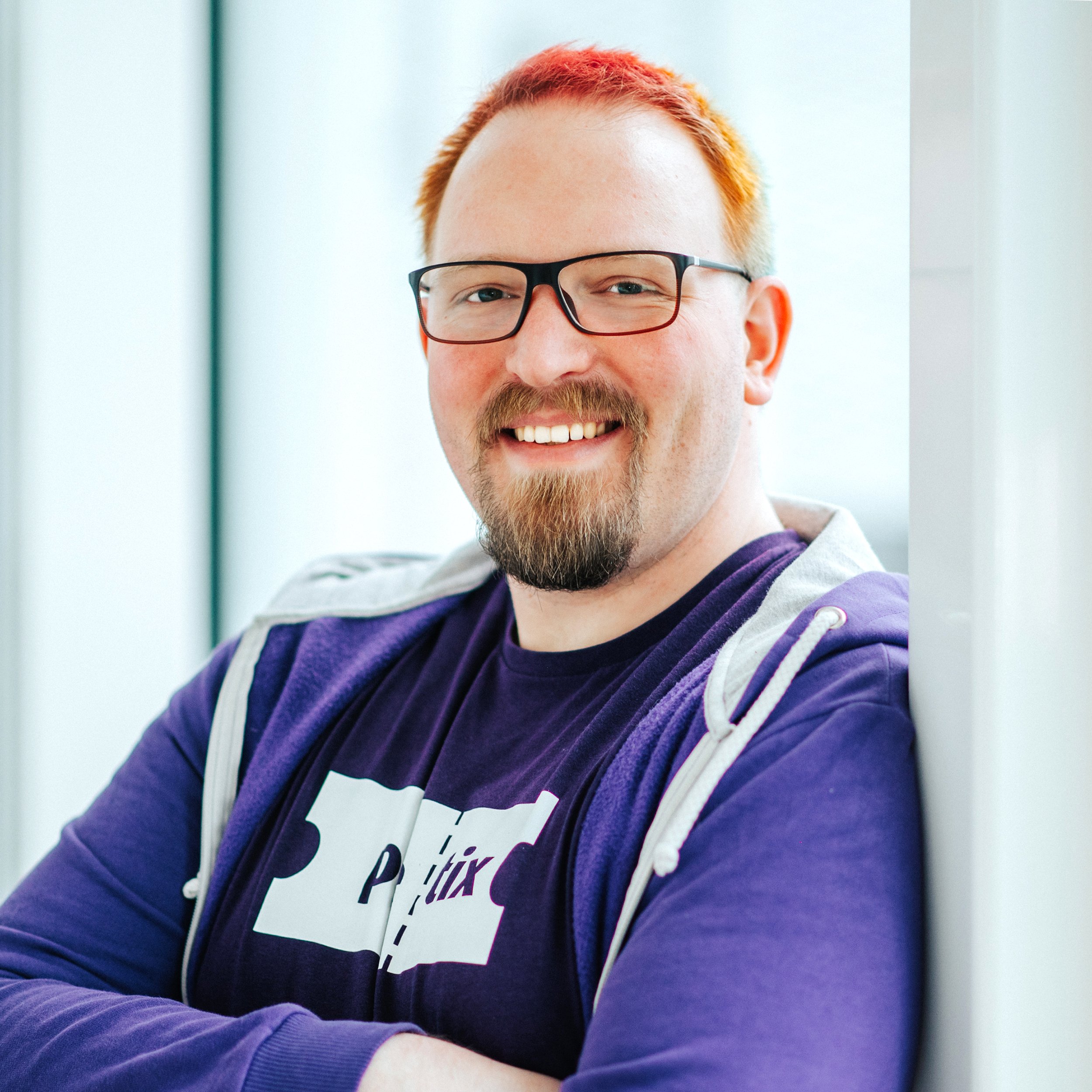 Dennis Lichtenthäler aus dem Venueless-Team. Dennis trägt ein pretix T-Shirt und einen pretix Hoodie. Er lächelt in die Kamera.