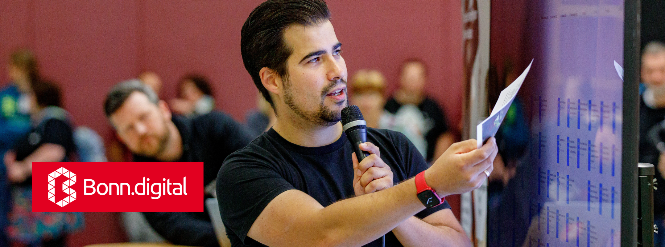 Sascha Foerster von Bonn.digital auf einer Bühne mit einem Mikrofon, daneben das Bonn.digital Logo